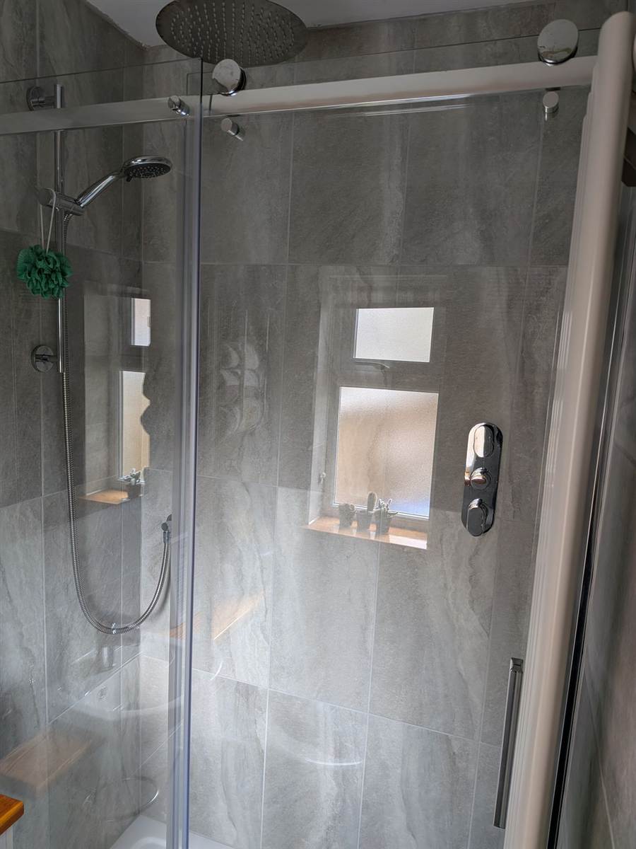 After — finished shower with frameless sliding door, rain head overhead, hand shower on riser and thermostatic valve